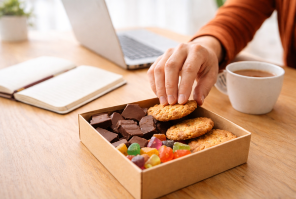 Envie de sucre sous stress au bureau : main prenant un biscuit près d’une tasse de café