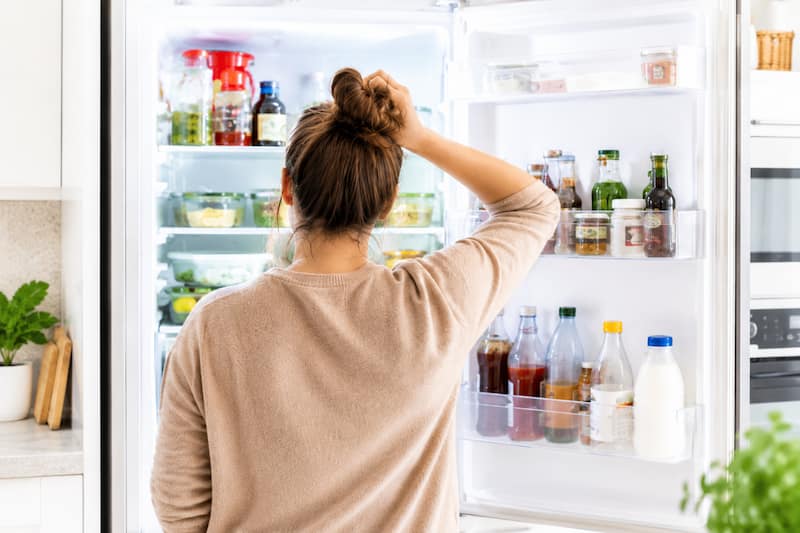 Femme hésitant devant son frigo après une journée chargée